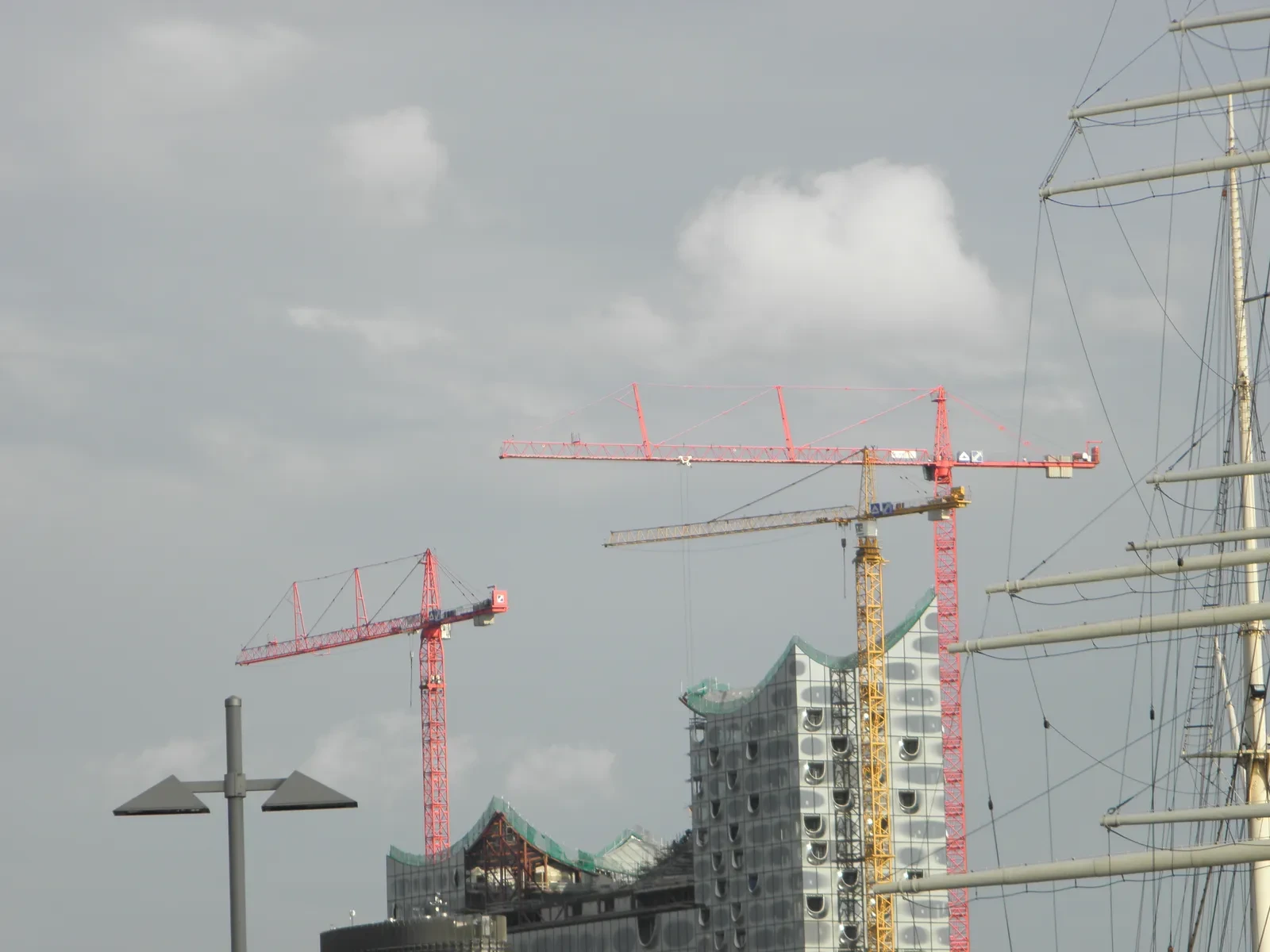 Blick auf eine Großbaustelle mit roten und gelben Turmdrehkranen vor bewölktem Himmel